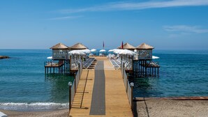 Un muelle de madera que conduce a bungalós sobre el agua, con sombrillas y sillas de descanso.