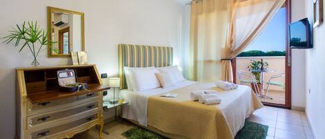 Habitación de hotel con cama, cómoda, espejo, televisor y balcón con una silla y planta.