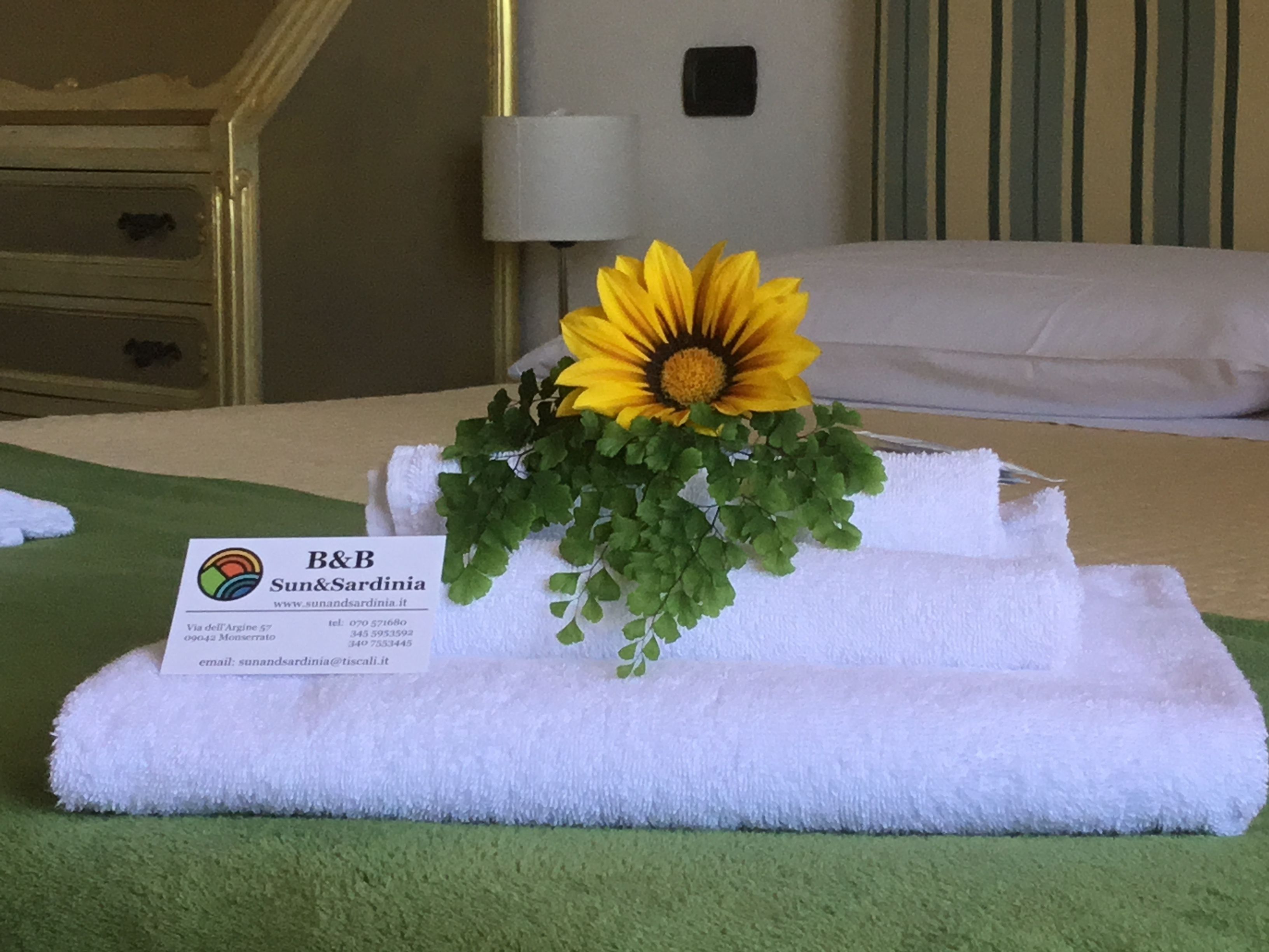 A neatly made bed with a white towel and a flower arrangement on top. A business card is placed on the towel.