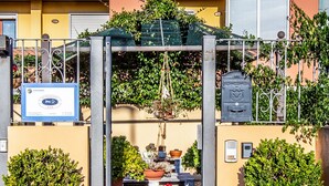 A gated entrance with a metal archway, potted plants, and a signboard. - Sun&Sardinia (Monserrato)