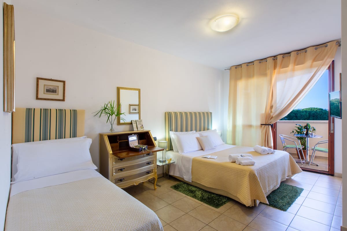 A hotel room with two beds, a wooden dresser, a small table with chairs, and a balcony with a view.