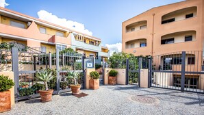 A courtyard with a gated entrance, potted plants, and buildings with balconies. - Sun&Sardinia (Monserrato)