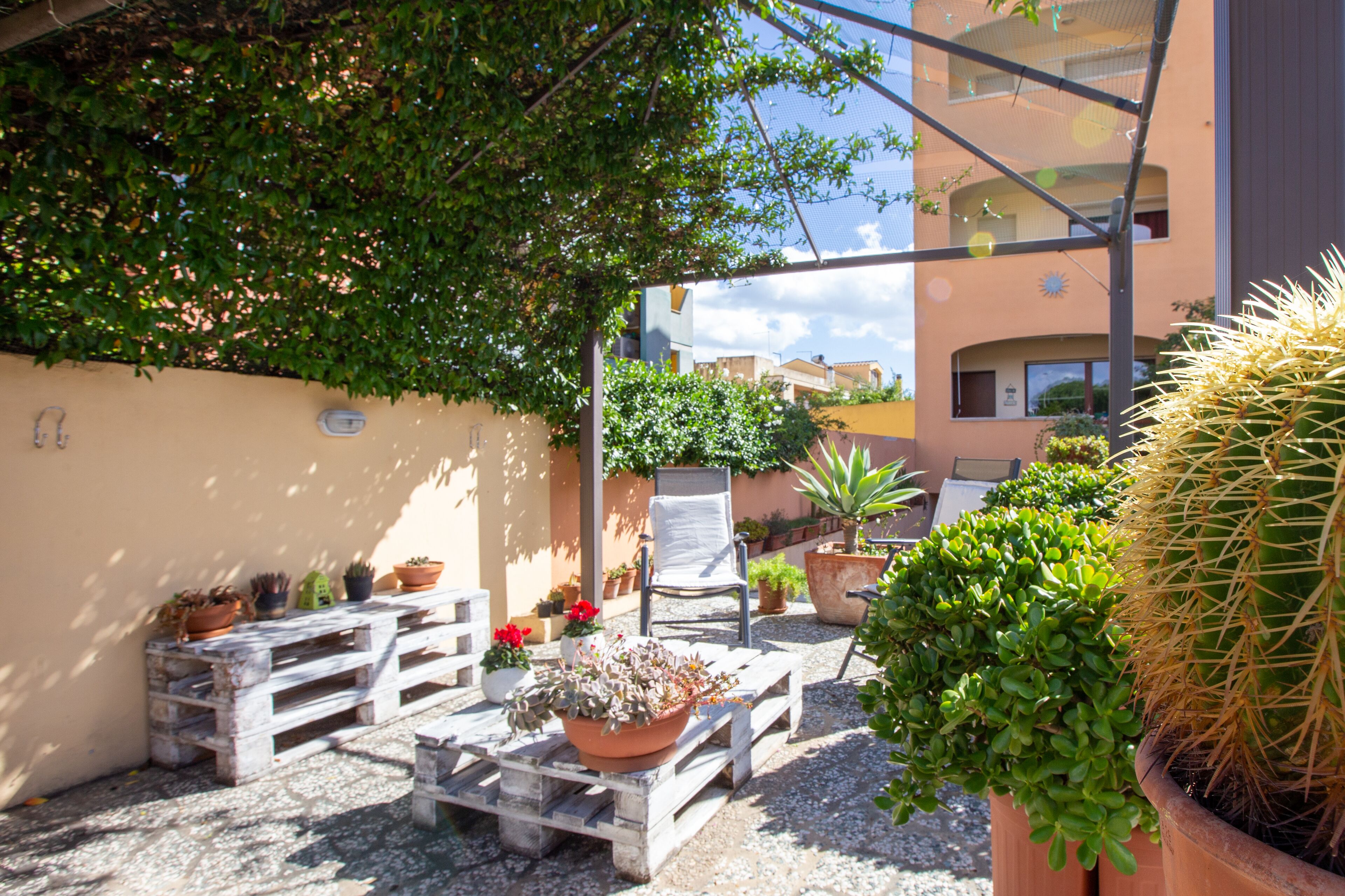 Un patio con plantas en macetas, un banco de madera y una silla.