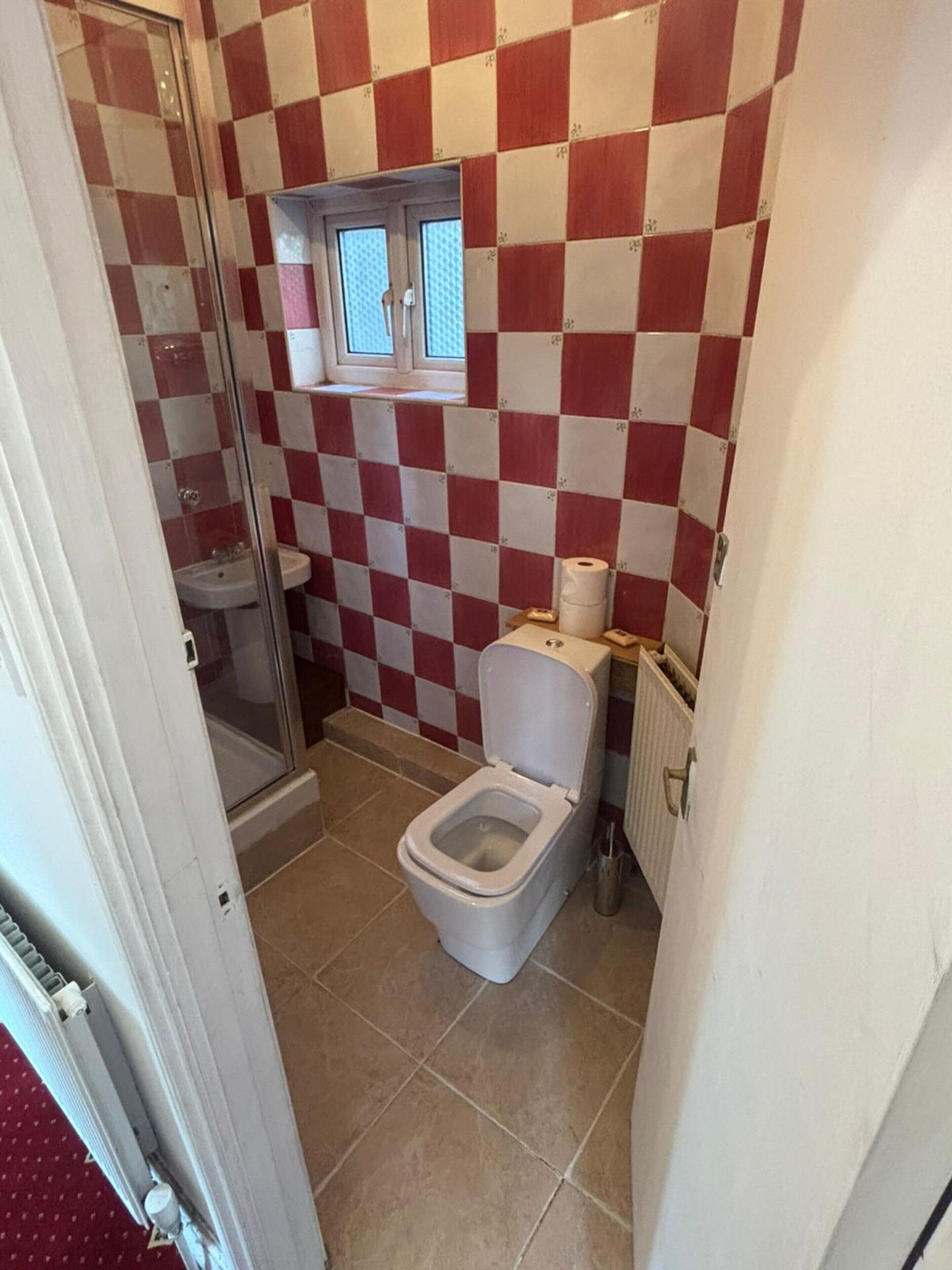 A small bathroom with a checkered red and white wall, a toilet, a sink, and a window above the sink.