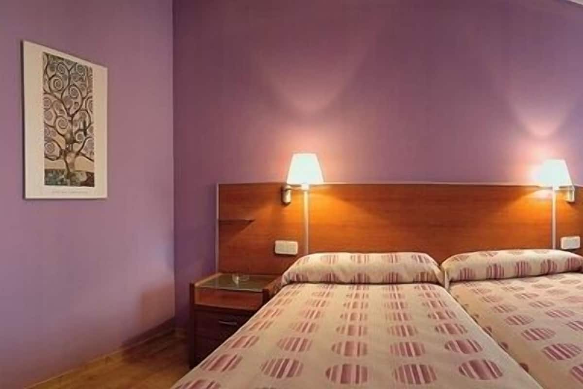 A hotel room with two beds, a wooden headboard, a desk, and a chair.
