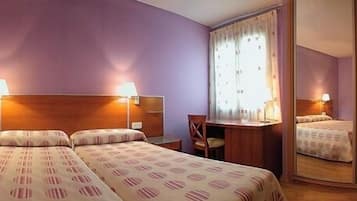 Habitación de hotel con dos camas, cabecera de madera, un escritorio y una silla.