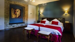 Una camera d'albergo con un letto grande, due comodini, un tavolino con sedie, una parete in pietra e un quadro.