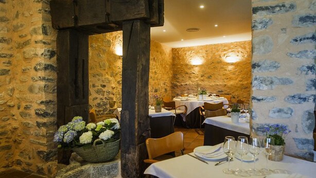 Un'accogliente sala da pranzo rustica con pareti in pietra, travi in legno e tavoli apparecchiati per un pasto.