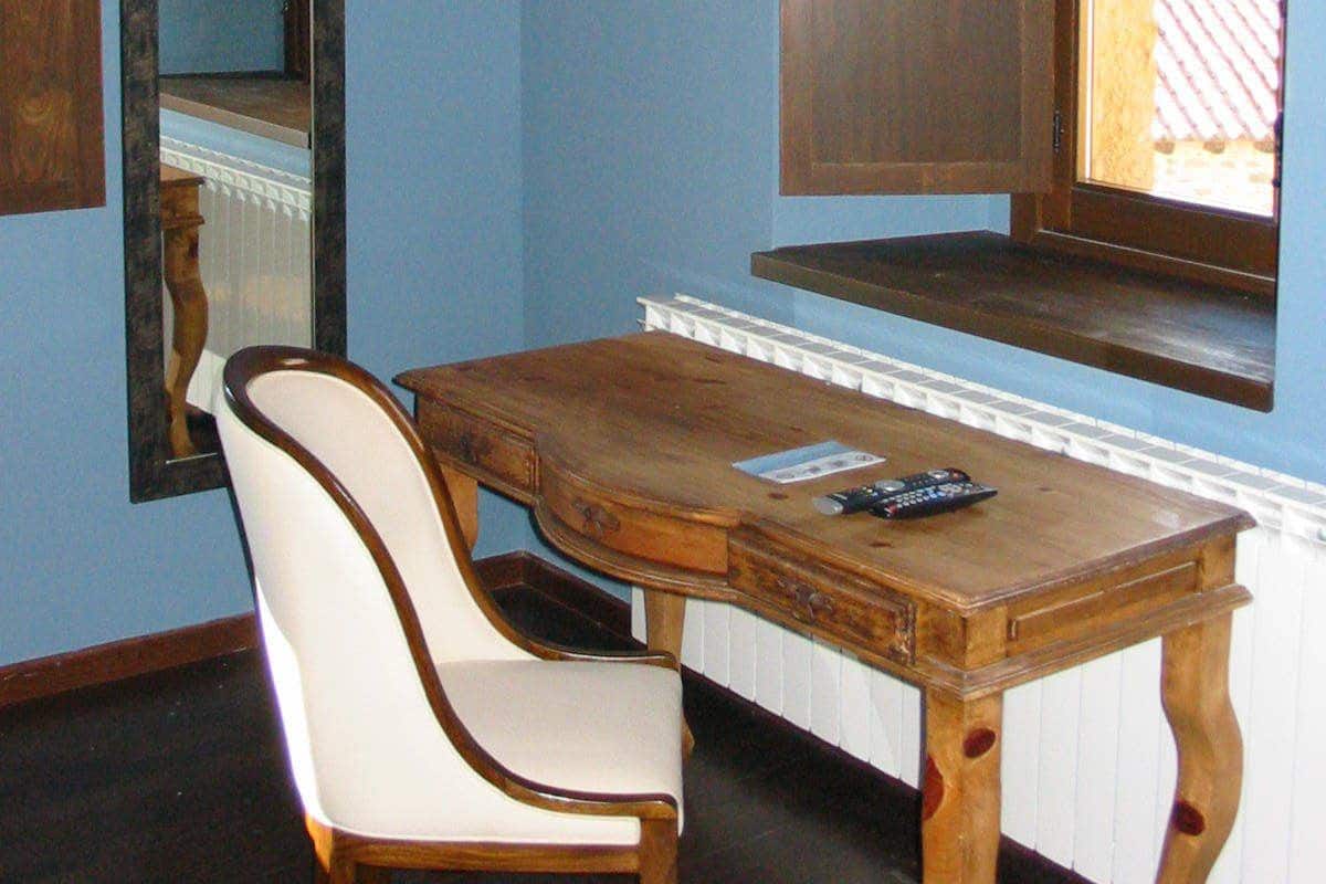 A room with a wooden table, a white chair, a mirror, and a window with a view of the outside.