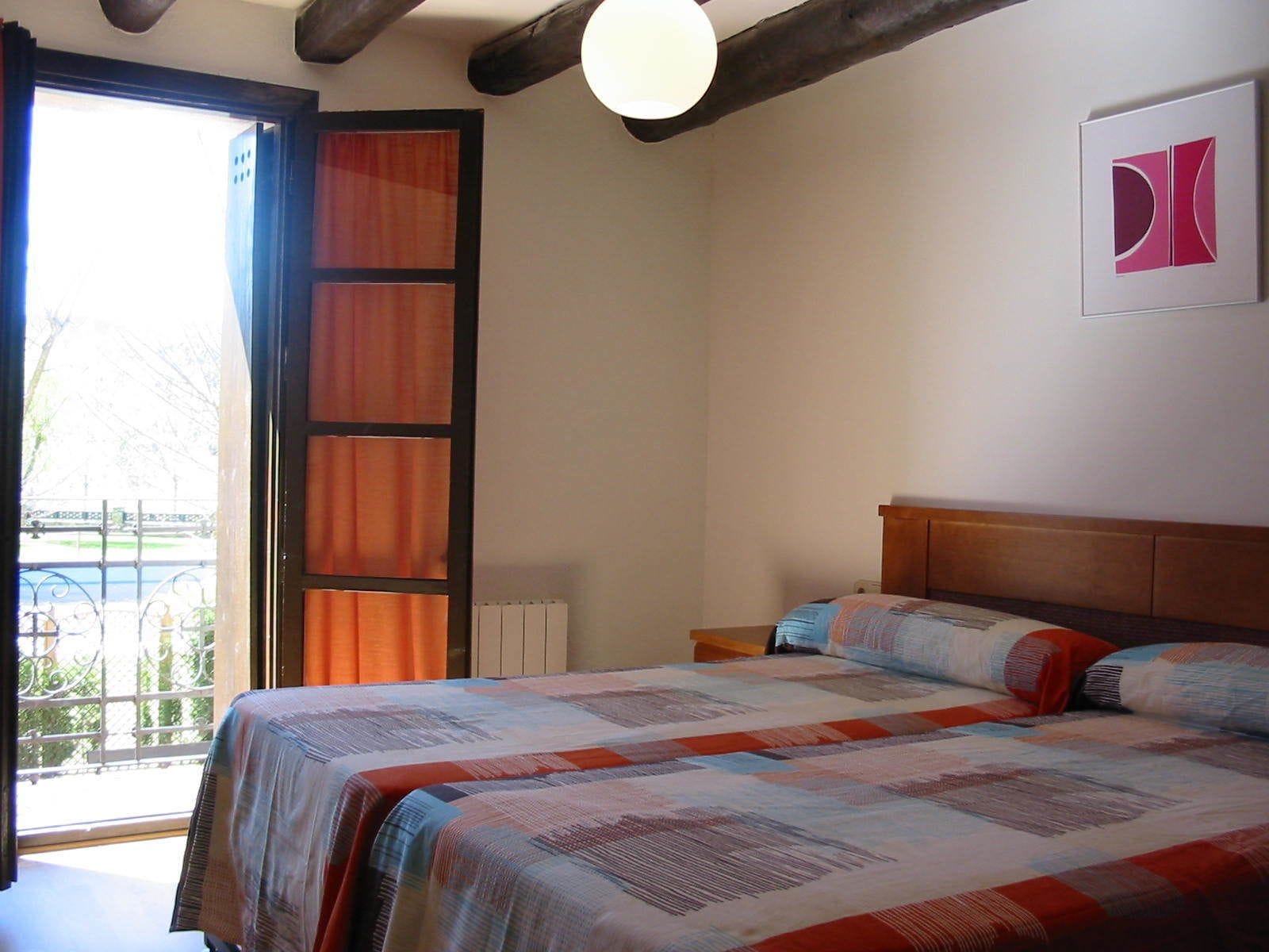 Une chambre à coucher avec un grand lit, une tête de lit en bois, un radiateur et une fenêtre avec des rideaux.