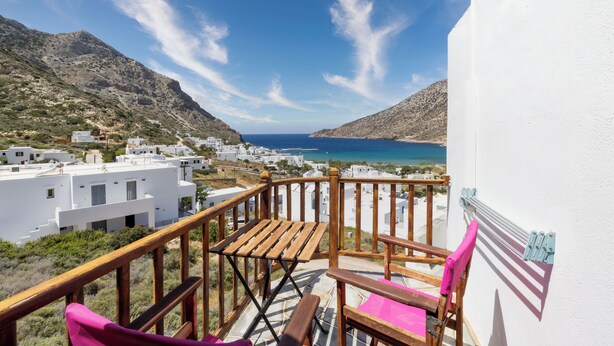 A balcony with a wooden railing, a folding table, and two chairs. - Froudi (Sifnos)