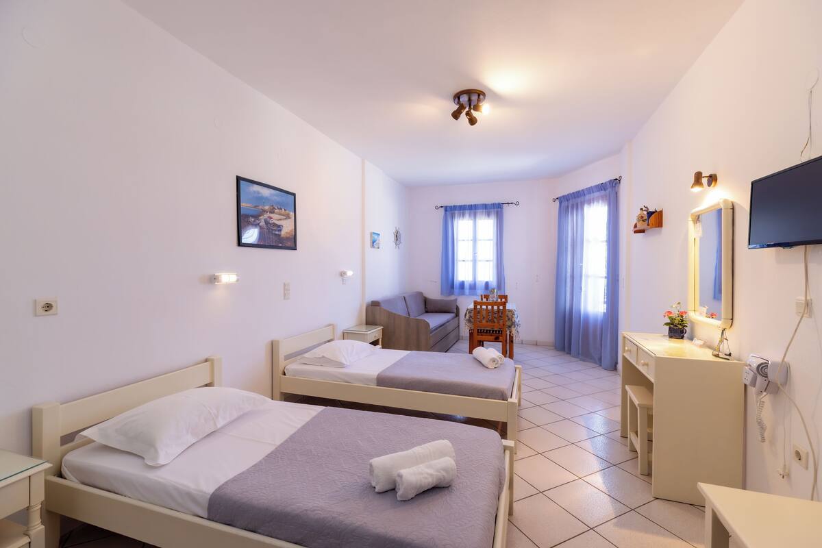 A hotel room with two beds, a desk, a chair, a TV, and a window with curtains.