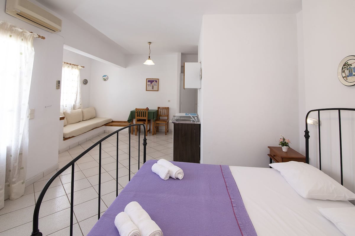 A compact hotel room with a bed, a small dining table, a sofa, and a kitchenette.