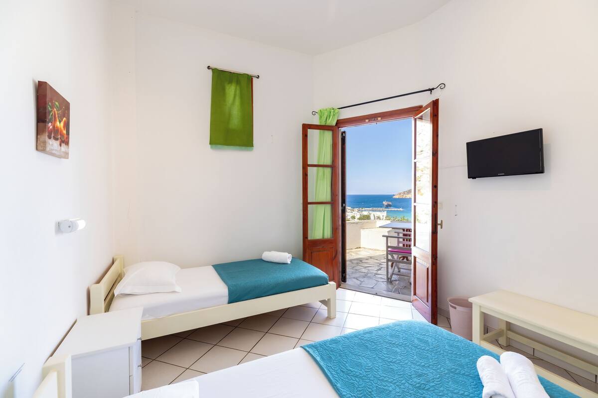 A room with two beds, a TV, and a view of the sea.