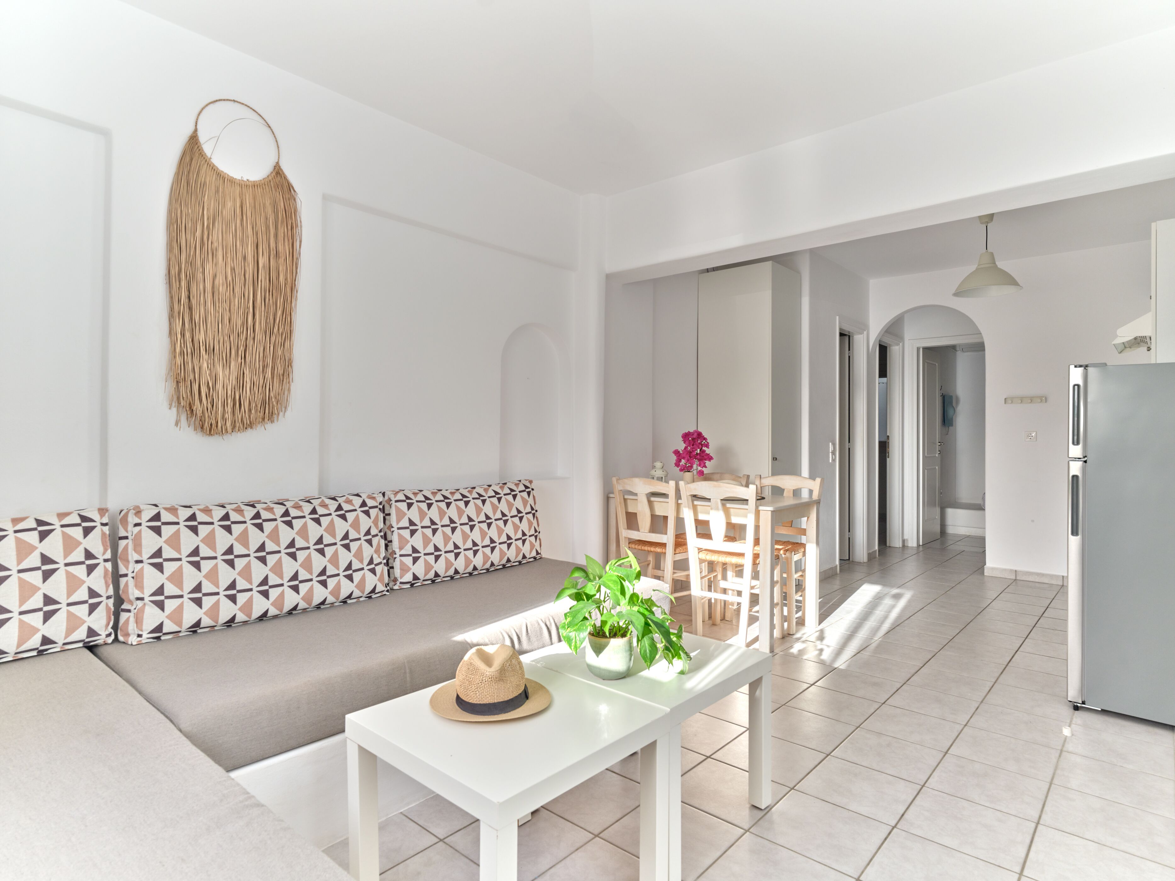 A modern living room with a sofa, a dining table with chairs, a kitchen area, and a hallway.