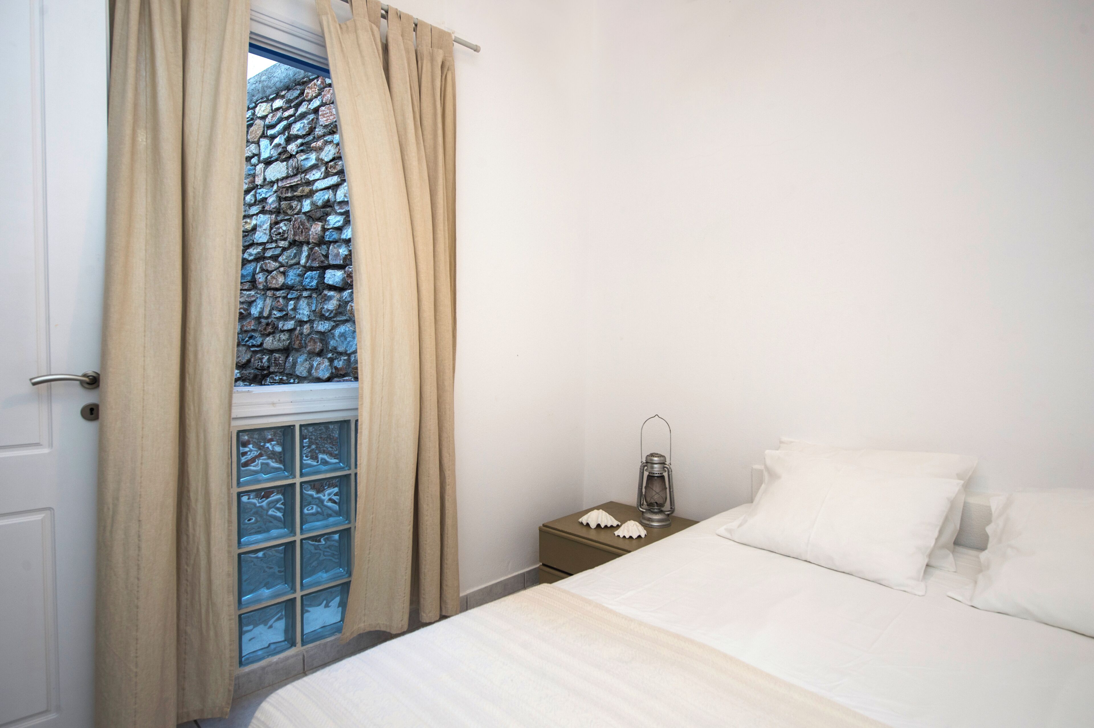Quarto com cama, mesa de cabeceira, lanterna e janela com cortinas.