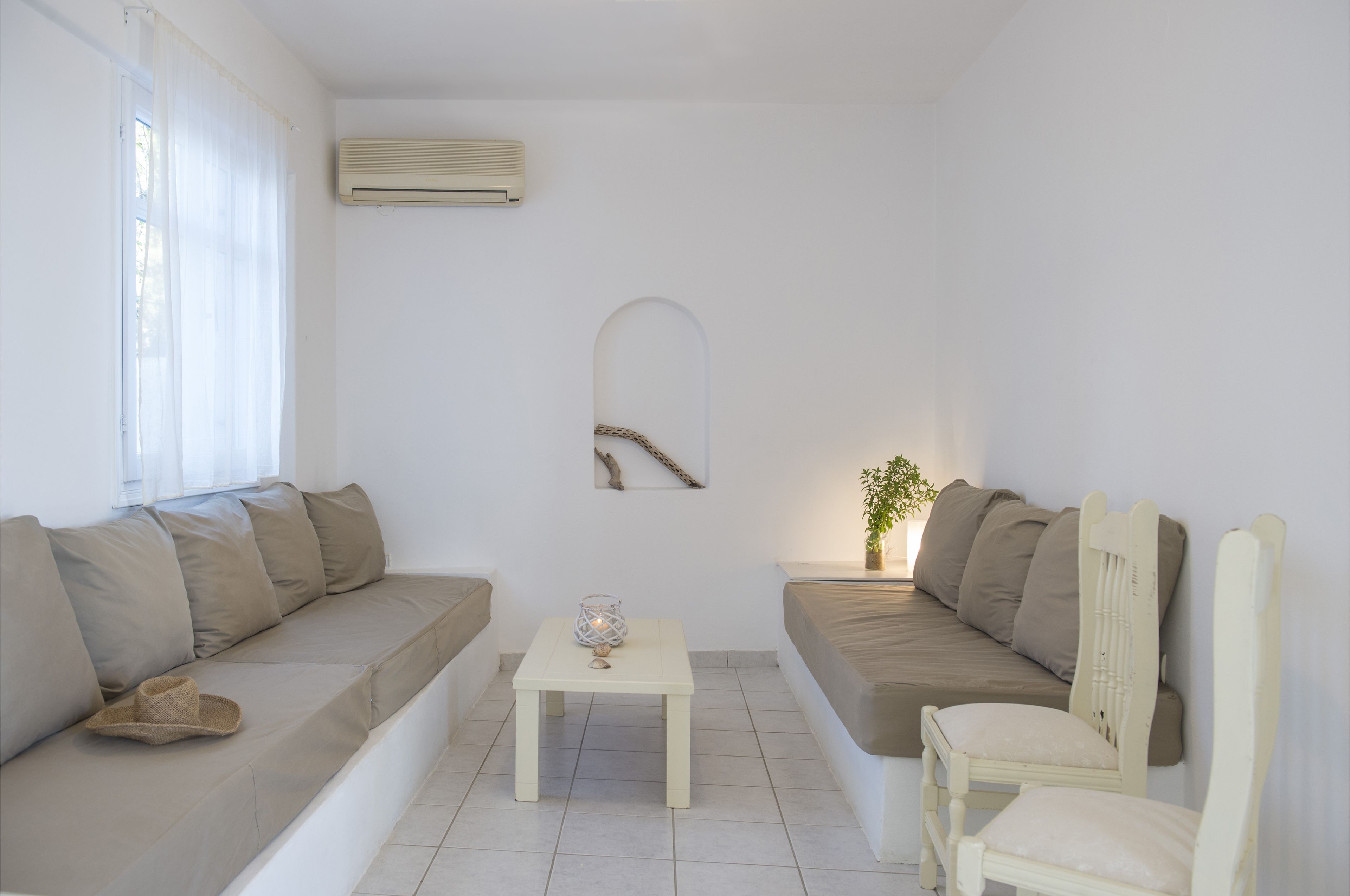 A minimalist living room with a beige sofa, a white armchair, and a small white table with a glass candle holder.