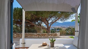 A balcony with a view of a tree, a stone wall, and distant mountains. - Cleopatra Seaside Homes Paros (Paros)