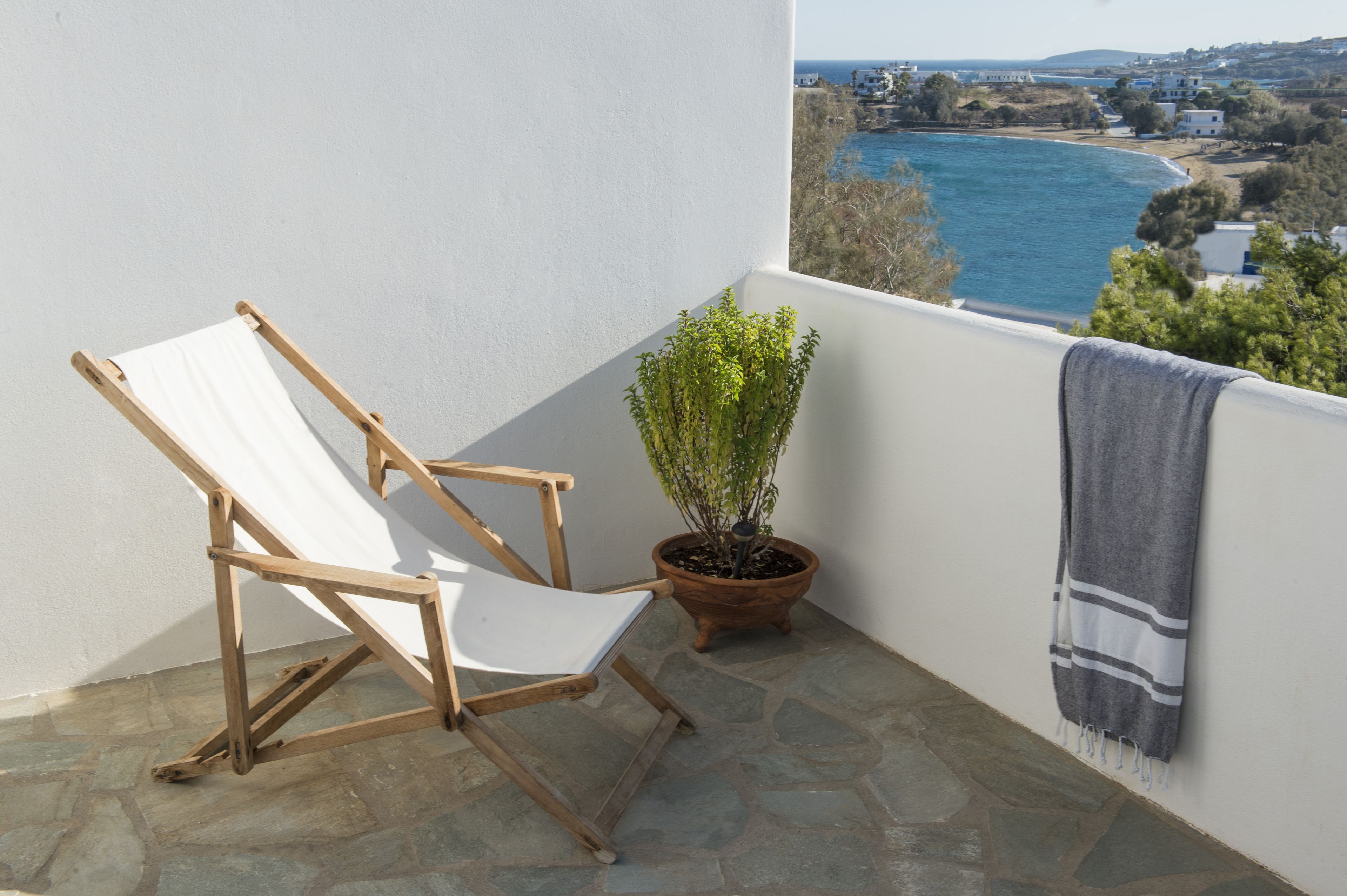 A balcony with a white chair, a potted plant, and a towel hanging on the railing.
