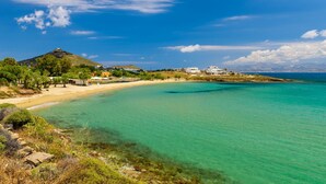 A coastal landscape with a clear turquoise sea, sandy beach, and a hill with buildings. - Cleopatra Seaside Homes Paros (Paros)