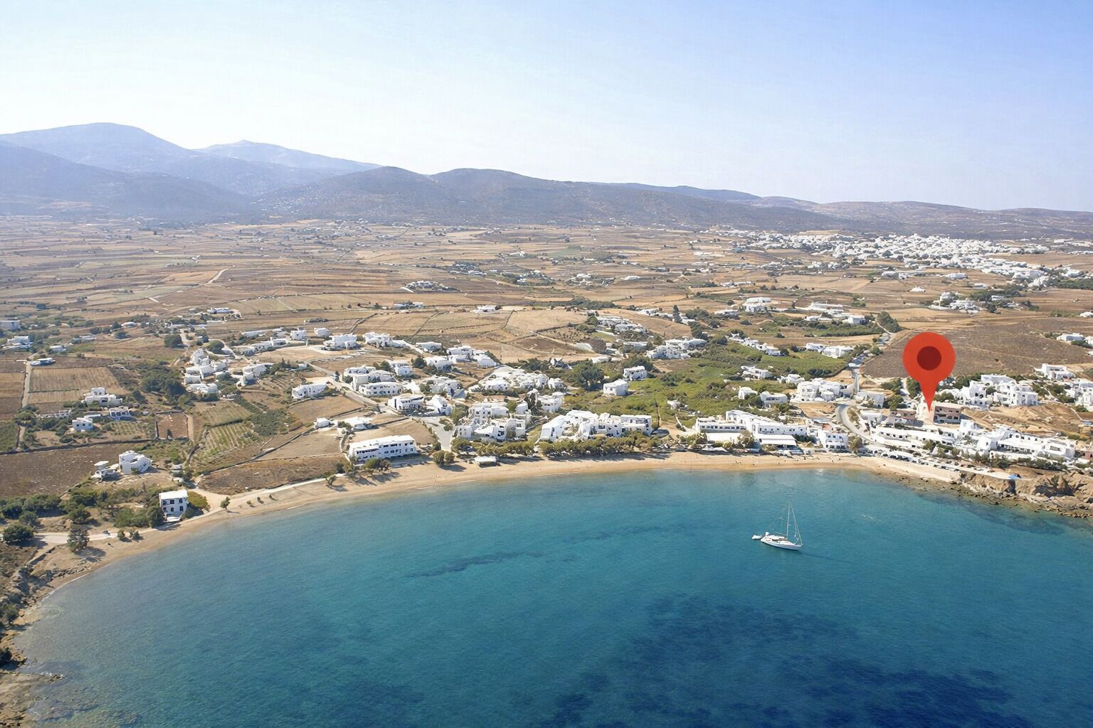 Vista aèria d'una ciutat costanera amb edificis blancs, una platja i un mar blau i tranquil.