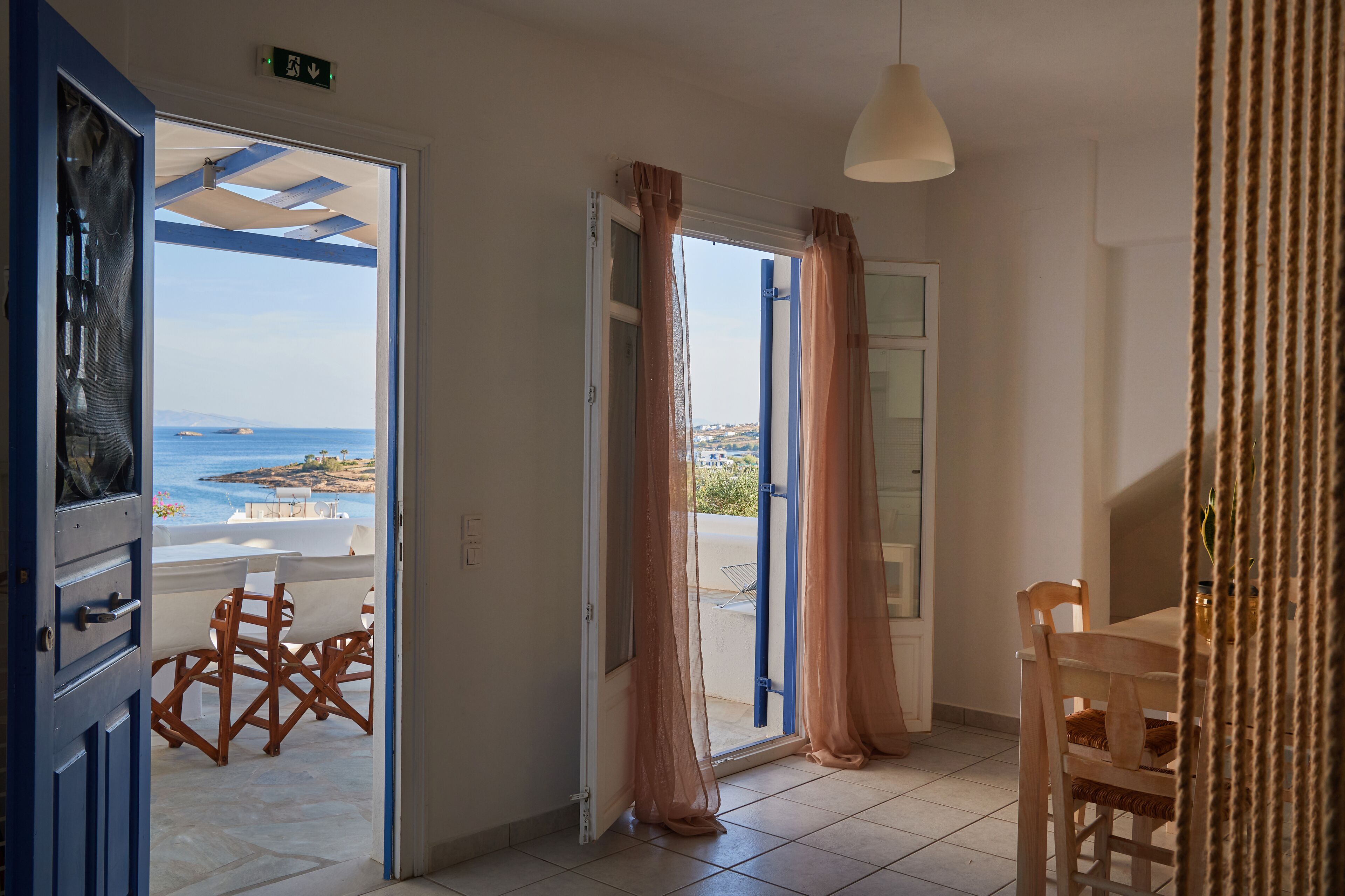 A room with a view of the sea, a dining area, and a door leading outside.
