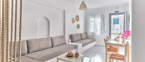 A modern living room with a sofa, a small table, and a dining area with chairs.