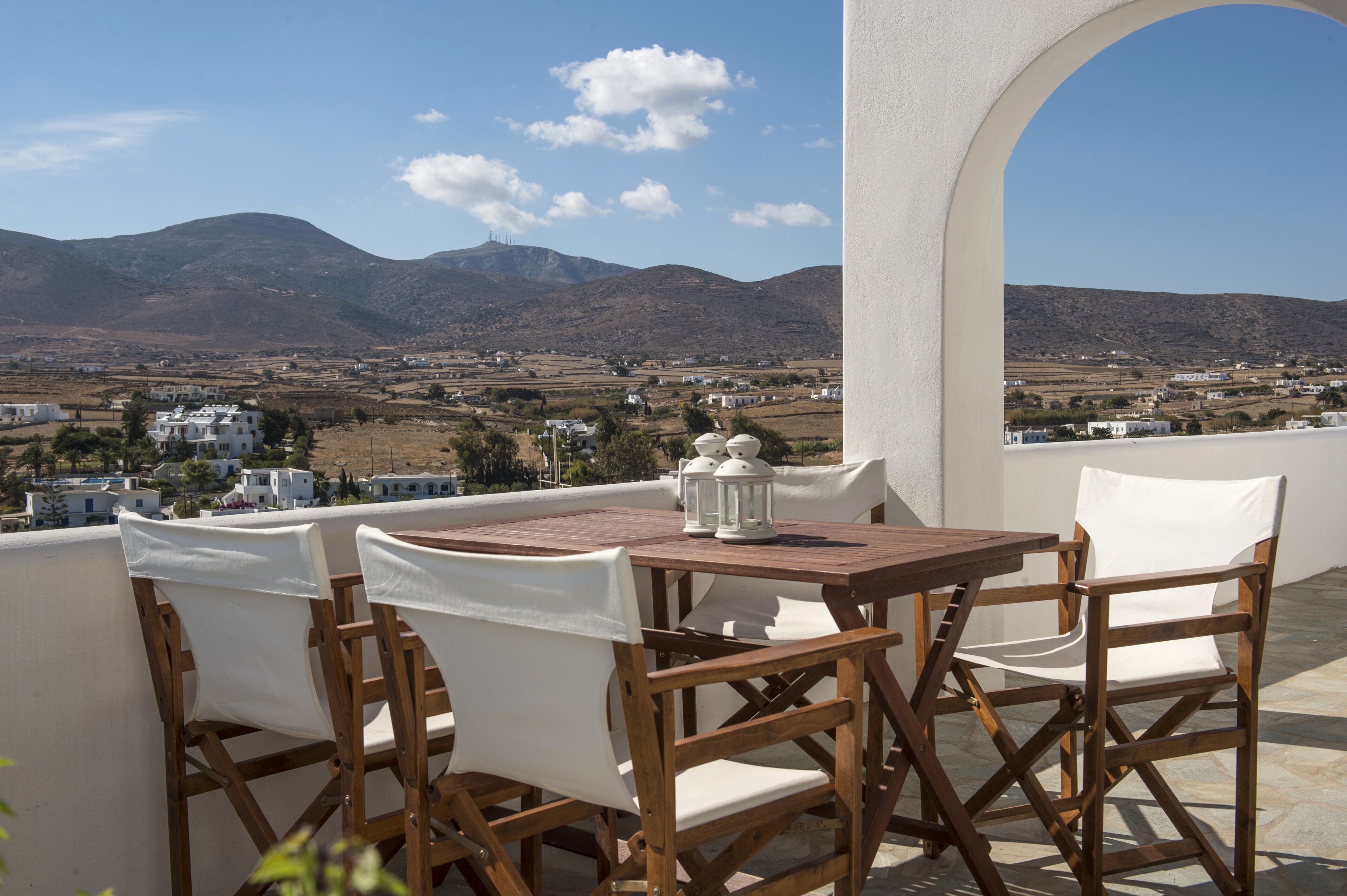 Eine Terrasse mit einem Holztisch und weißen Stühlen mit Blick auf eine Berglandschaft mit weißen Gebäuden.