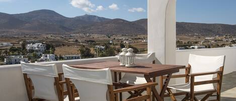 Eine Terrasse mit einem Holztisch und weißen Stühlen mit Blick auf eine Berglandschaft mit weißen Gebäuden.