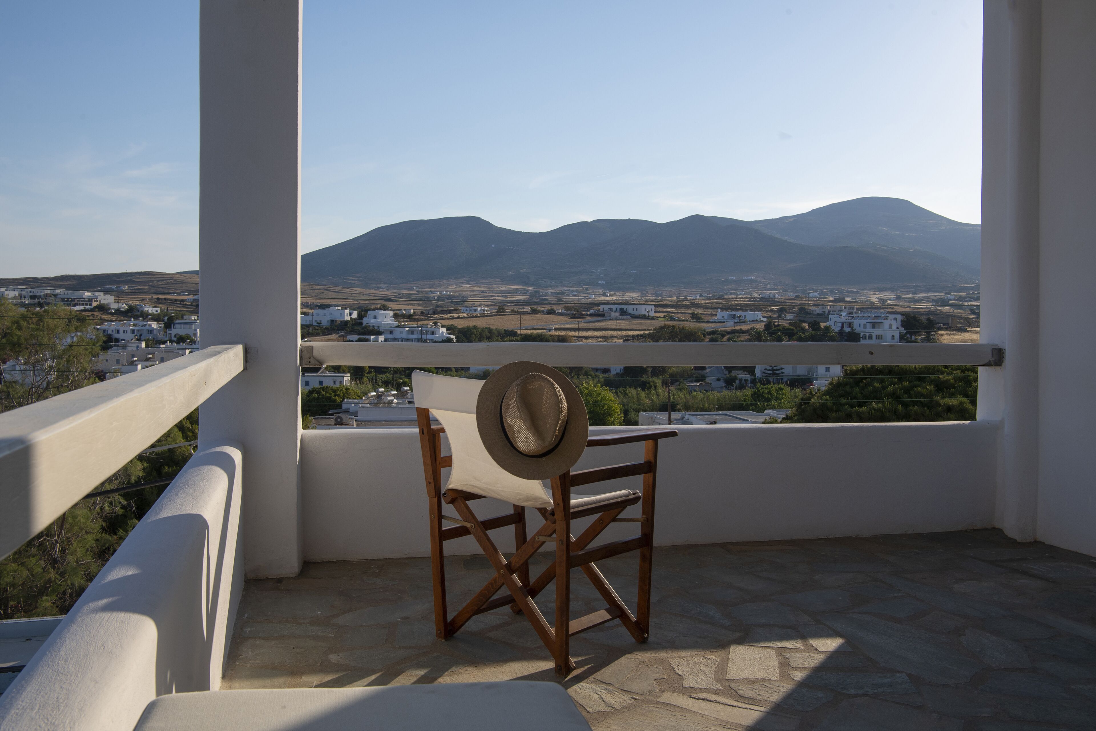 A balcony with a view of a mountain range, a white chair, and a hat on the chair.