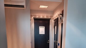 A hotel hallway with a wooden floor, a trash bin, a bed with a blanket, and a door with a sign. - Halltorps Gästgiveri (Borgholm)