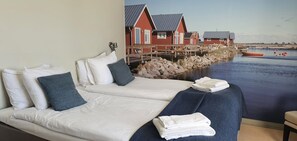 A hotel room with a bed, pillows, a blanket, and a view of a waterfront with houses. - Halltorps Gästgiveri (Borgholm)