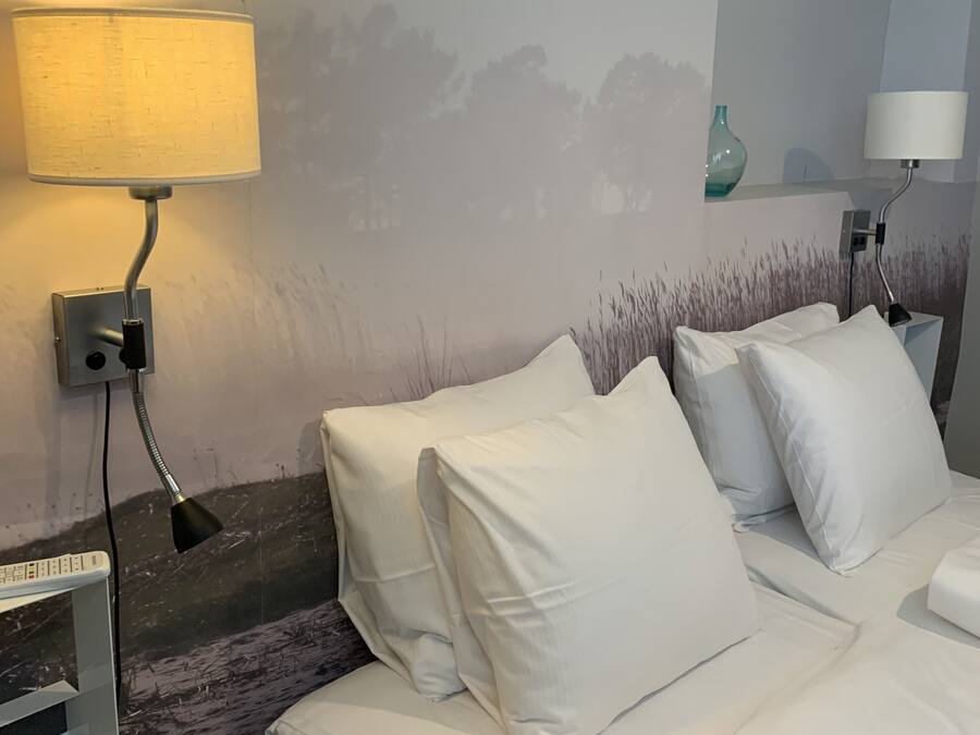 Habitación de hotel con cama, dos lámparas de noche, un control remoto y televisor montado en la pared.