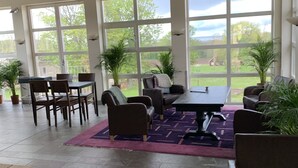 A spacious room with large windows, a dining table, several chairs, and potted plants. - Halltorps Gästgiveri (Borgholm)