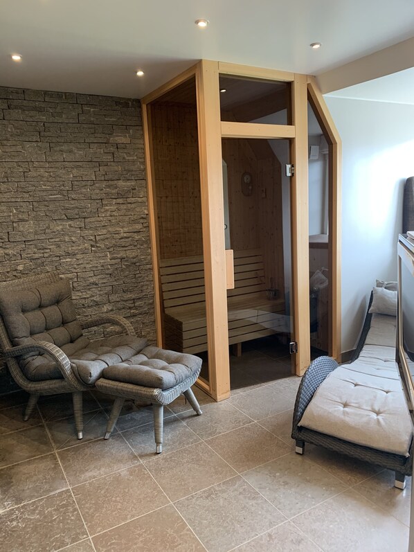 Una habitación con pared de piedra, sauna de madera y dos sillones de mimbre.