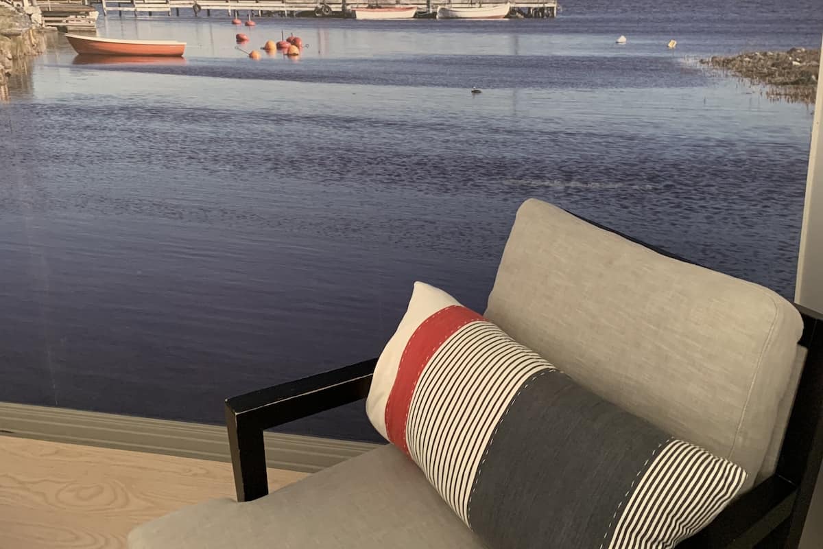 Ein Balkon mit Blick auf einen ruhigen Hafen, der Boote und eine Mole im Hintergrund zeigt.