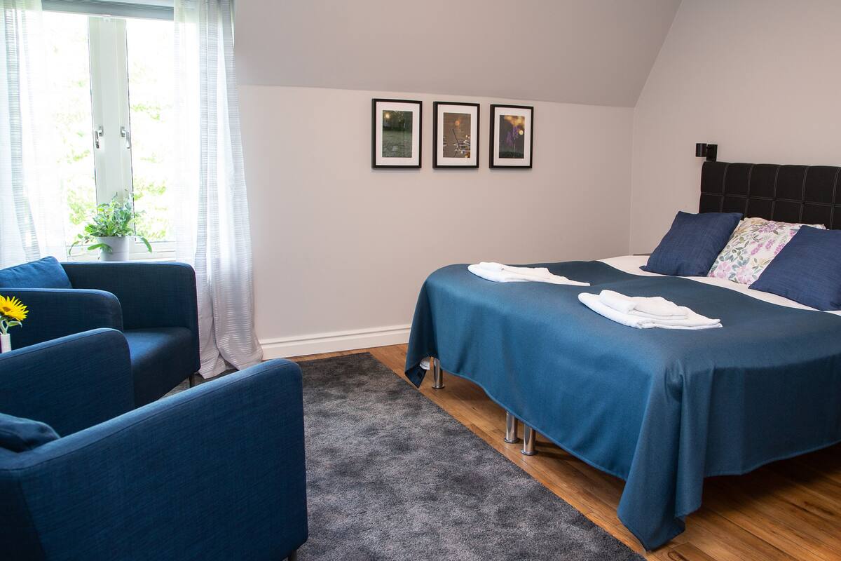 Ein Schlafzimmer mit einem Bett, einer Couch, einem Fenster mit Vorhängen und drei gerahmten Bildern an der Wand.