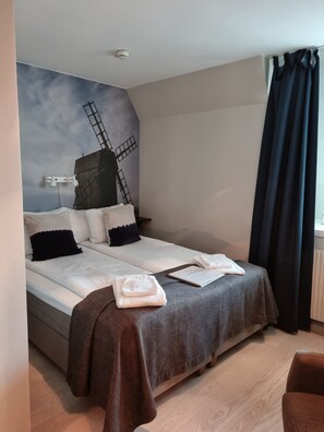 Habitación de hotel con cama, un mural de molino y ventana con cortinas, además de suelo de madera.