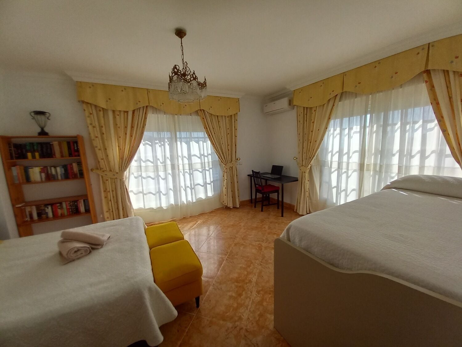 Une chambre d’hôtel avec deux lits, un bureau avec un ordinateur portable, une bibliothèque et une fenêtre avec des rideaux.