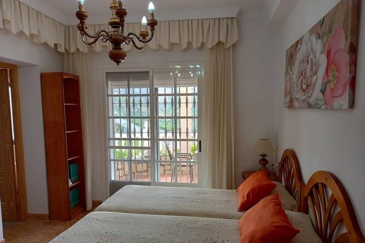 A bedroom with two beds, a chandelier, a large window with a view, and a painting on the wall.