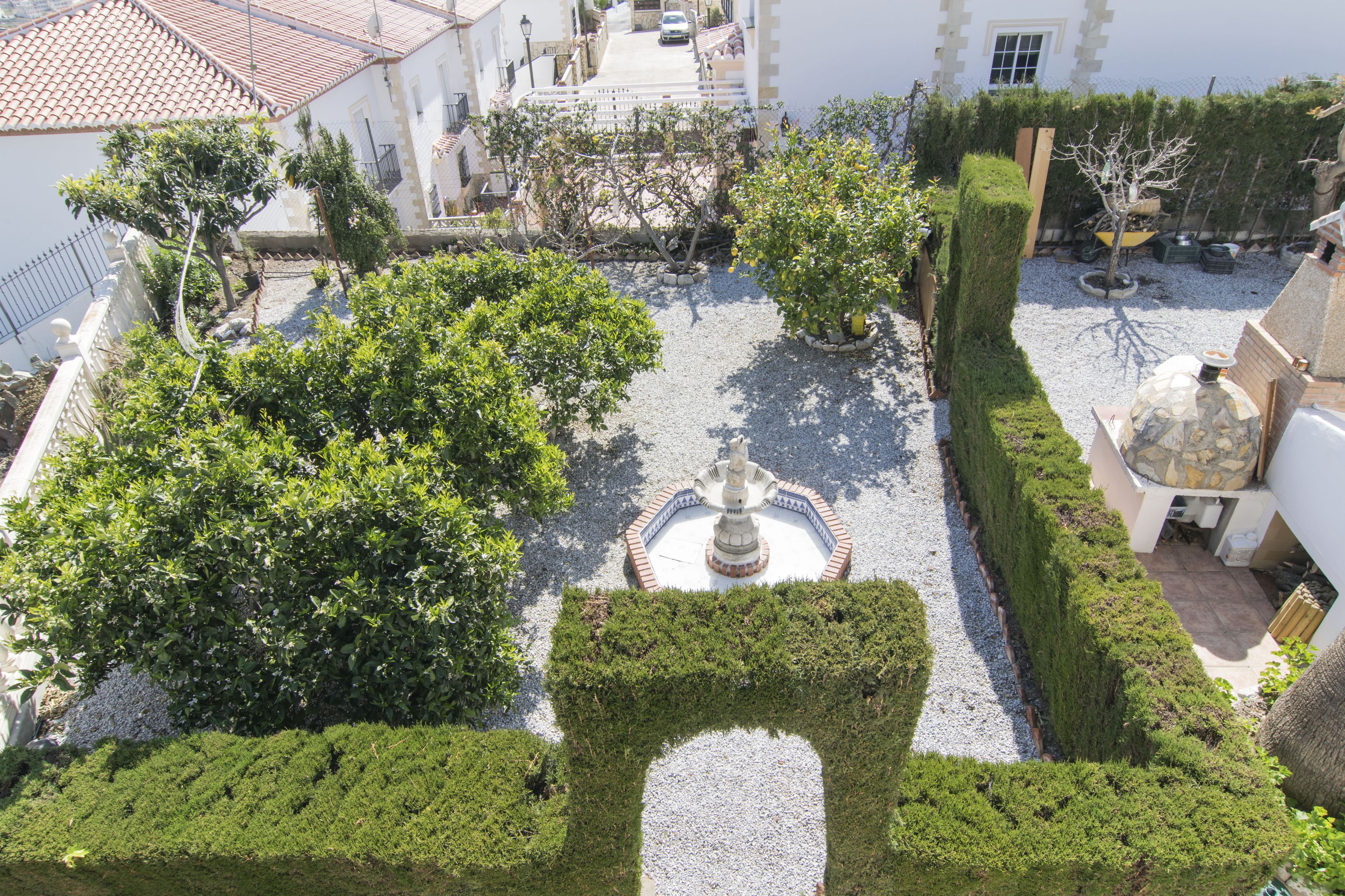 Un patio con una fuente central, rodeado de setos y árboles bien cuidados.