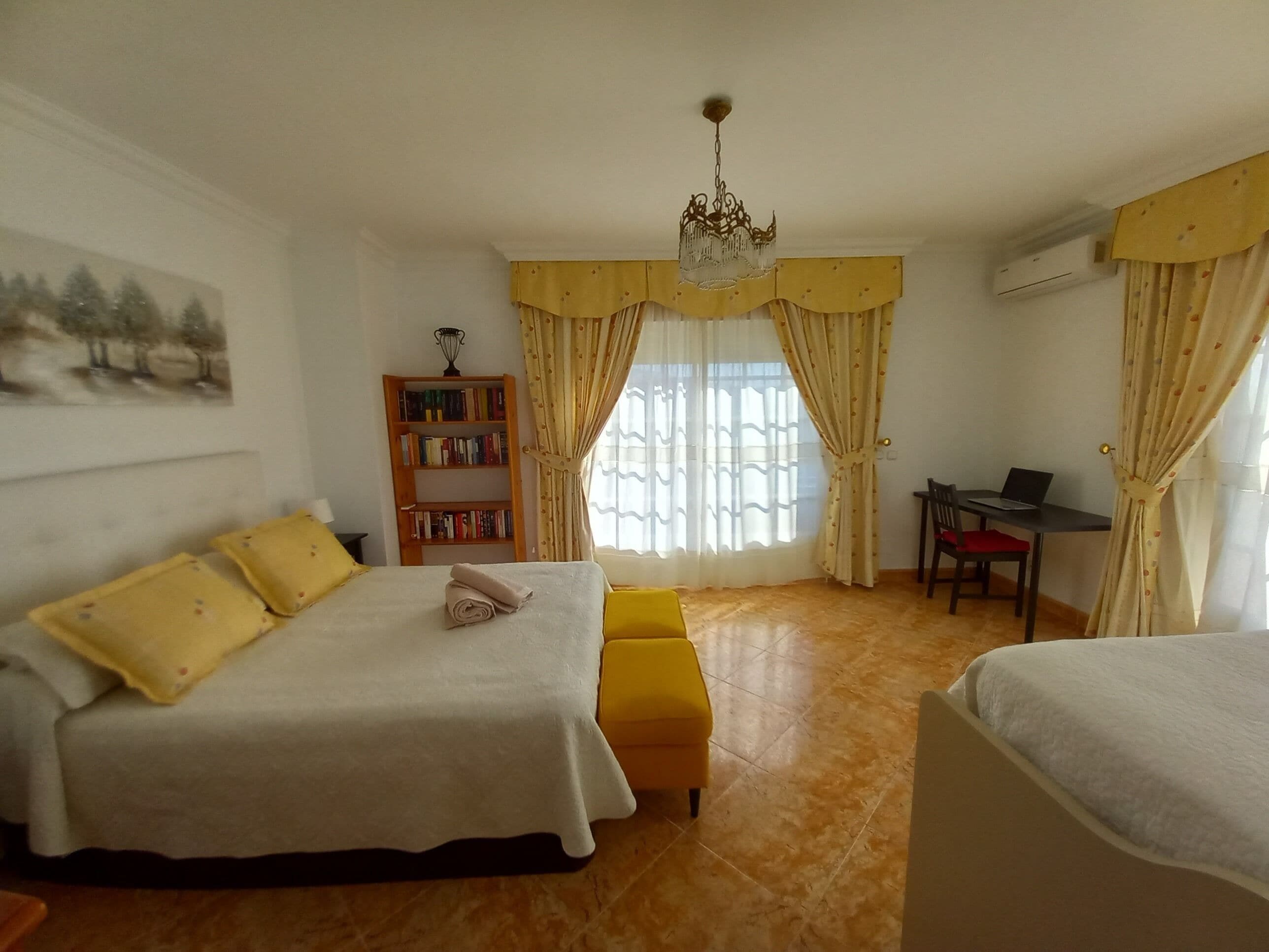 A bedroom with a bed, a desk, a bookshelf, and a chandelier.