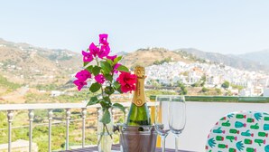Een tafel met een champagnefles, twee glazen en een vaas met roze bloemen op een balkon met uitzicht op een stad.