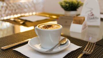 Une tasse de café posée sur une soucoupe, avec une cuillère et une fourchette sur la table.