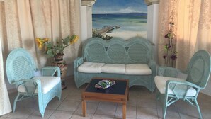Ein Zimmer mit Blick auf einen Strand, eine Couch, zwei Sessel, ein Couchtisch und eine Topfpflanze.