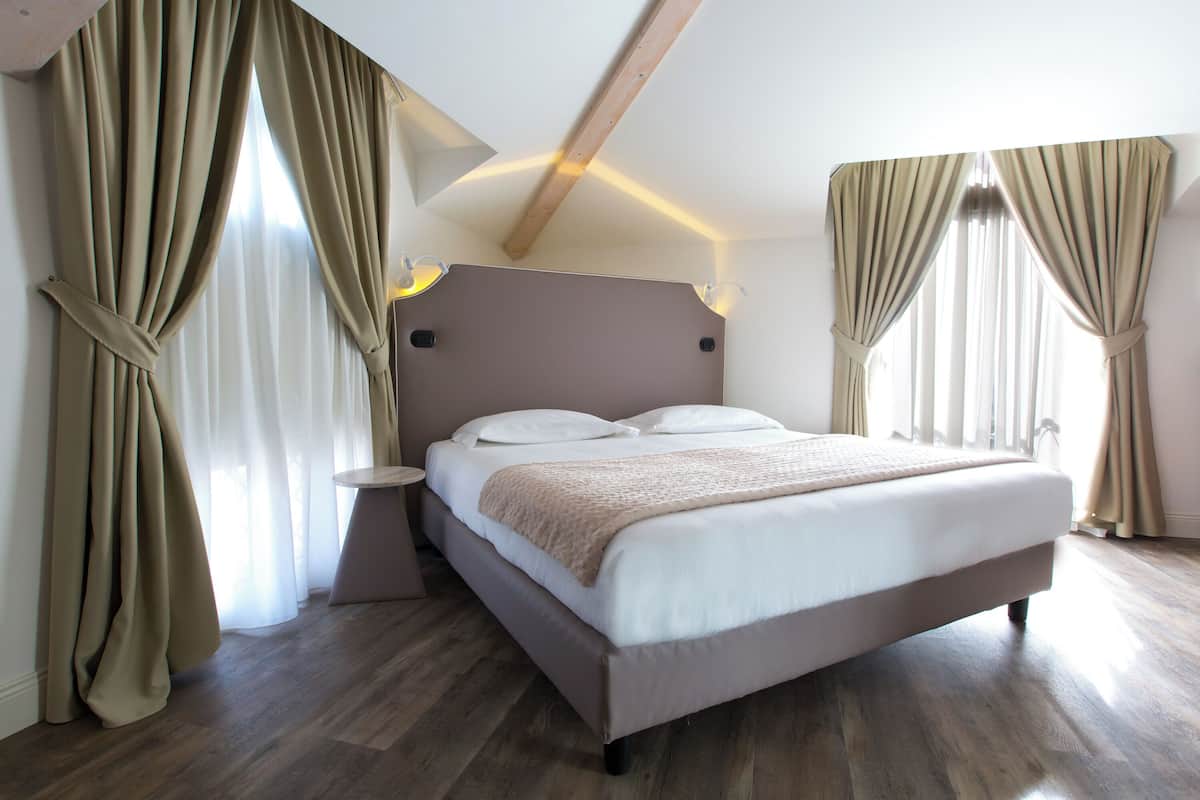 Ein modernes Schlafzimmer mit einem großen Bett, beigen Vorhängen und einem Holzbalken an der Decke.