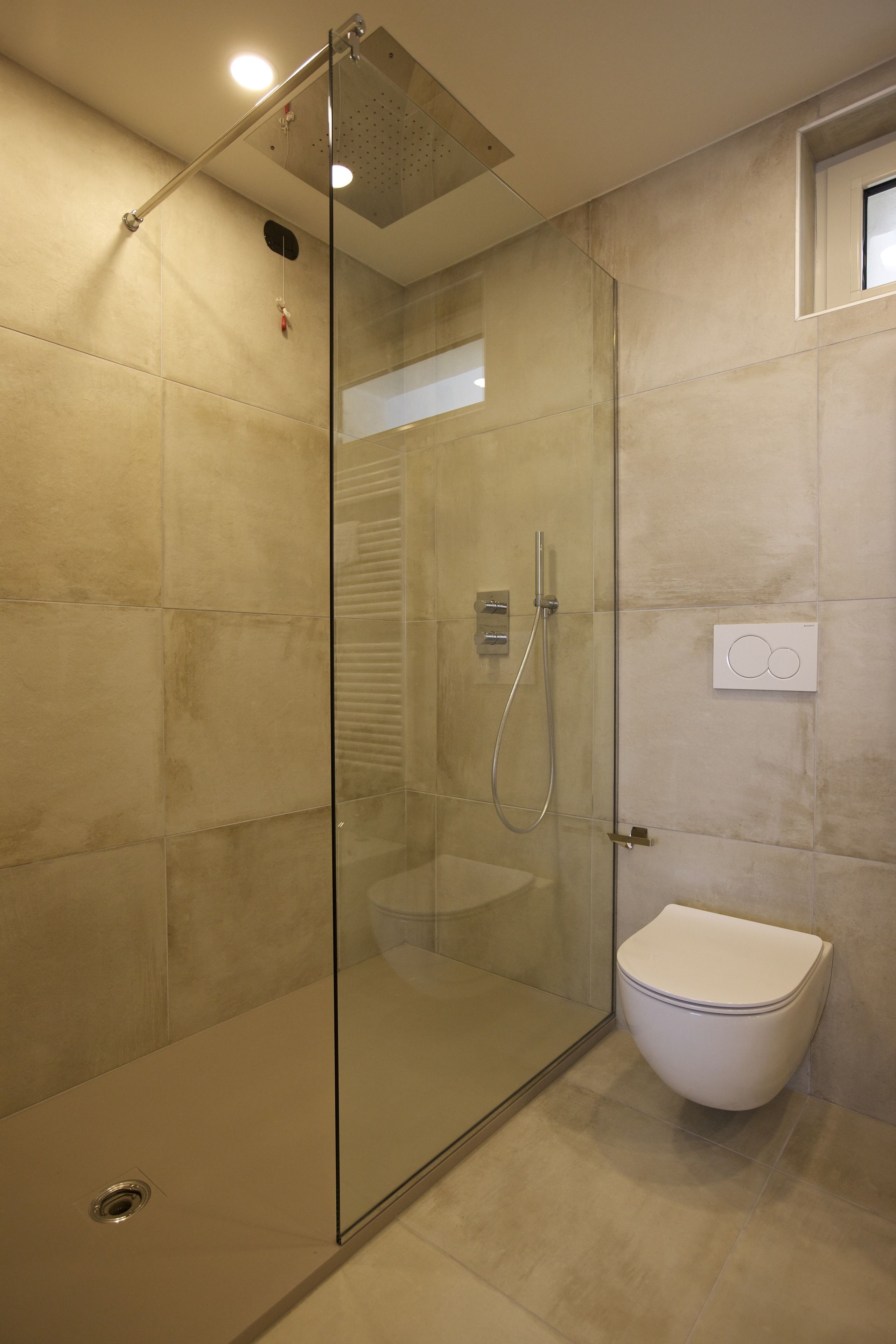 A modern bathroom with a glass-enclosed shower, a toilet, and a wall-mounted control panel.