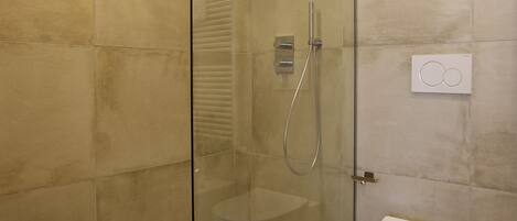 Uma casa de banho moderna com chuveiro em cabine de vidro, sanita e painel de controlo fixado na parede.