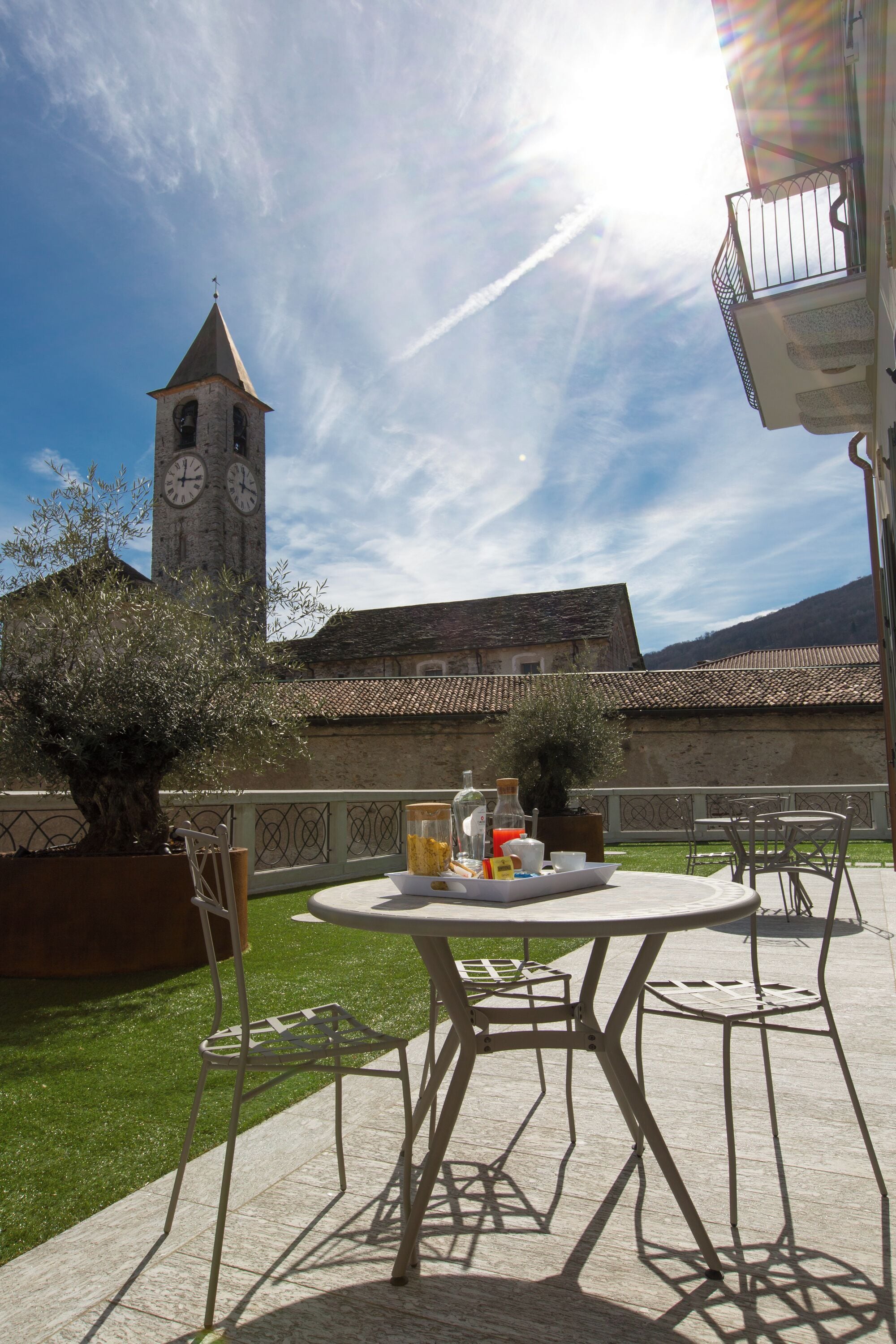 An outdoor patio with a round table and chairs, a clock tower in the background, and a clear sky.