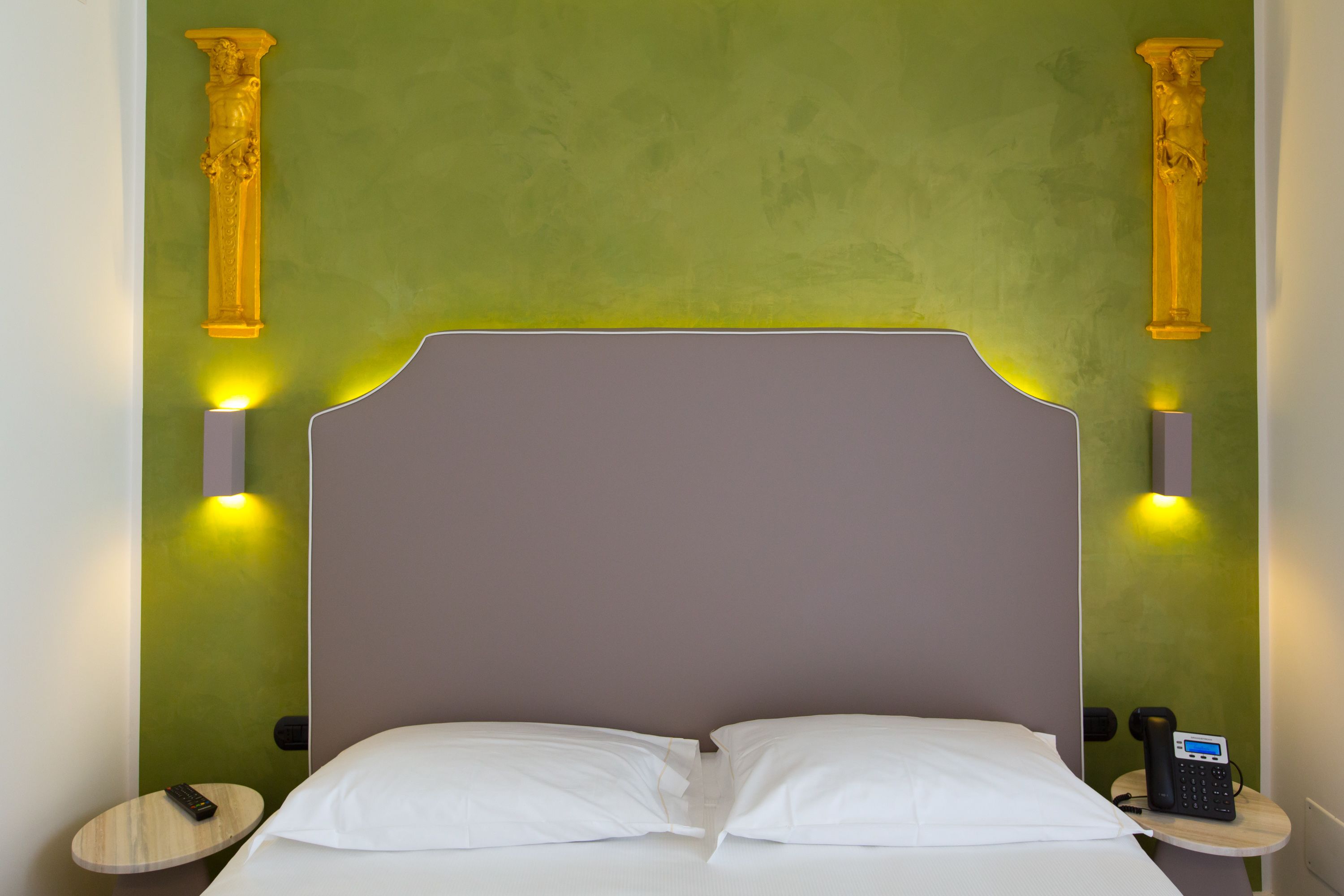 A bed with white pillows and a grey headboard in a room with green walls and two columns.